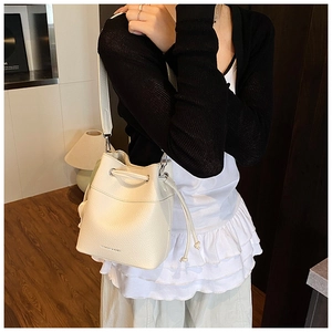 Close-up of creamy white bucket bag with drawstring closure and litchi grain texture
