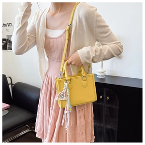 Detail of yellow lychee texture handbag with a colorful rainbow tassel charm and strap