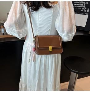 Detail of brown vintage crossbody bag with lace charm and gold buckle on white dress
