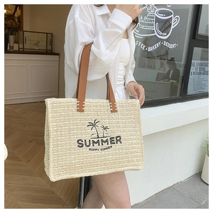Detail of hand-woven straw tote bag with leather handles and embroidered summer palm motif