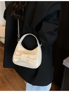 Sac demi-lune crème élégant avec grand nœud et bandoulière chaîne porté sur un blazer