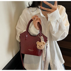 Dettaglio di una borsa a secchiello bordeaux retrò con logo dorato e ciondolo a orsetto