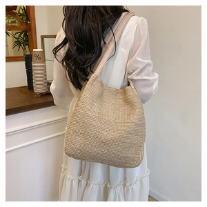 Close-up of a hand-woven straw tote bag with a wide shoulder strap in a cafe setting