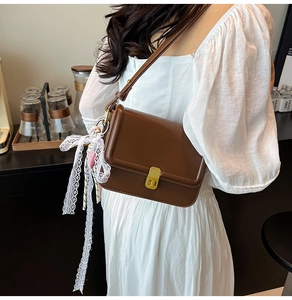 Detail of brown leather square crossbody bag with gold lock and white lace bow