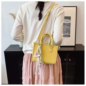 Detail of yellow lychee leather handbag with rainbow charm and printed ribbon accessory