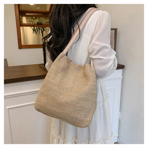 Close-up of beige woven tote bag with wide fabric strap on a model in white dress