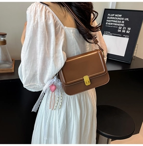 Detail of brown leather crossbody bag with gold metal clasp and lace heart charm decoration