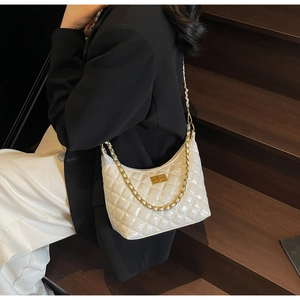 Detail of white quilted half-moon bag with gold chain and clasp on a black blazer
