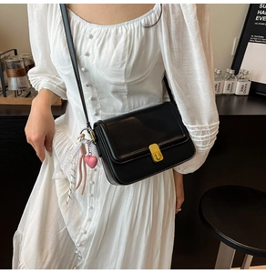 Detailed view of a black leather crossbody bag with a gold lock and pink heart charm
