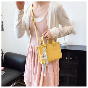 Detail of yellow lychee-textured tote bag with woven tassel and adjustable shoulder strap