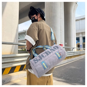 Outdoor street style view of a grey cylinder travel bag with blue and yellow straps