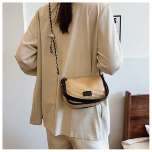Detail of woven straw saddle bag featuring black leather trim and metal chain strap