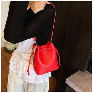 Detail of red lychee grain leather bucket bag with drawstring and silk scarf charm accessory