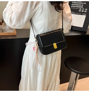 Detail of black glossy leather crossbody bag with gold lock and white lace charm decor