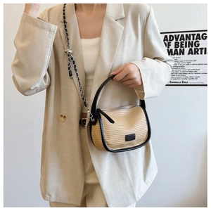 Detail of woven straw saddle bag with black leather trim and metal ball chain strap