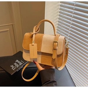 Detail of a two-tone patchwork handbag featuring woven texture and decorative buckle