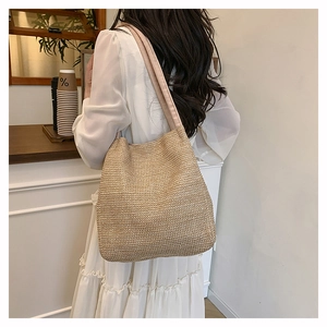 Detail of a large woven straw tote bag with wide khaki fabric strap shown on a shoulder