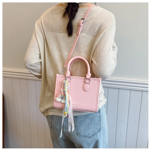 Detail of pink pebbled leather handbag with rainbow charm and decorative ribbon