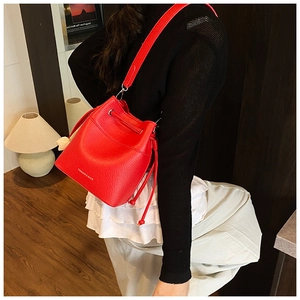 Detail of red bucket bag with litchi grain texture and gold fashion lettering