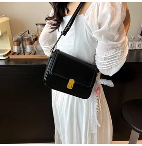 Detail of black leather square bag featuring golden turn-lock and pink heart pendant