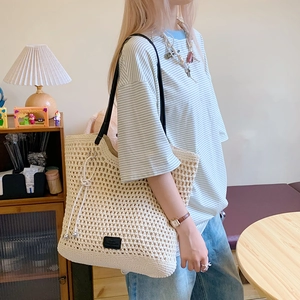 Detail of hollow crochet texture on a beige woven tote bag with black leather shoulder straps