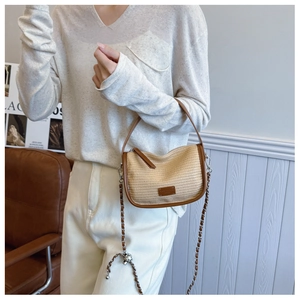 Close-up of woven straw shoulder bag with brown leather trim and metal brand logo