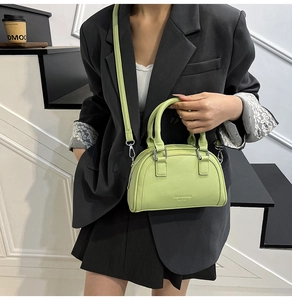 Détail d'un sac bowling vert clair en cuir grainé porté par un mannequin en costume noir