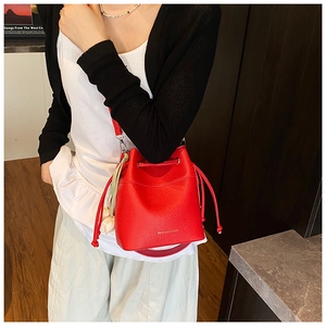 Detail of red bucket bag in litchi grain leather with flower pendant and shoulder strap