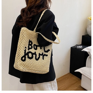 Détail du sac cabas en maille beige avec broderie Bonjour porté par un mannequin chic
