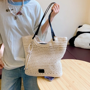 Detail of cream woven tote bag featuring black leather handles and white knot charm