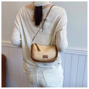 Detail of woven straw saddle bag with brown leather trim and metal chain strap