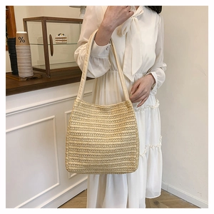 Detail of a beige woven straw tote bag with wide shoulder strap in a minimalist setting