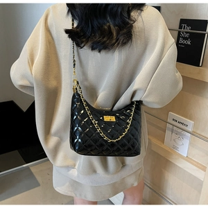 Detail of black quilted patent leather hobo bag with gold chain on model in cozy sweater