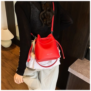 Detail of red bucket bag with lychee pattern texture, drawstring closure and floral charm