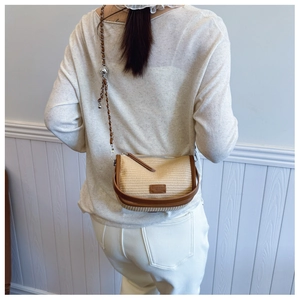 Detail view of a woven straw half-moon crossbody bag with brown leather trim and metal chain