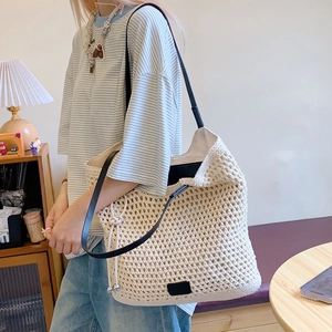Detailed macro view of woven cream beach tote bag with thin black leather shoulder strap
