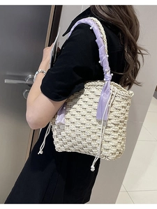 Woven bucket bag with cream straw finish, purple ribbon and pearl accents on shoulder strap