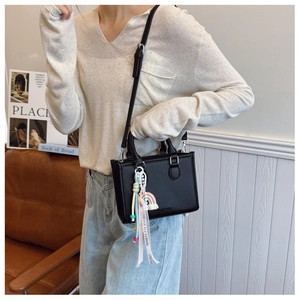 Close-up of black lychee-textured crossbody bag with colorful charms on a beige outfit