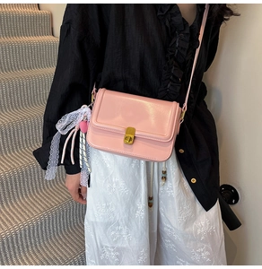 Detail of pink crossbody bag featuring gold rotary lock and lace heart pendant accessory