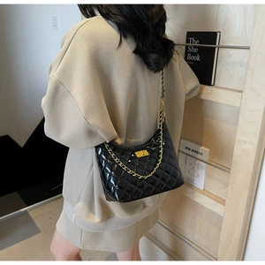 Detail of black quilted patent leather bag with gold chain strap and square buckle