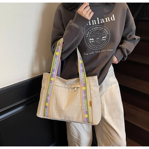 Detail of beige tote bag showing textured nylon fabric and contrast lettered strap