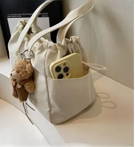 Detail of cream canvas drawstring tote with side pocket, plush bear, and phone for scale