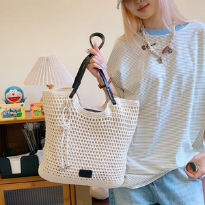 Close-up of beige crochet woven tote bag with black leather handles and tassel detail
