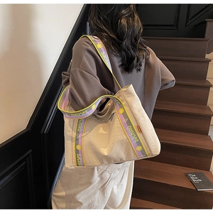 Close-up of a large beige canvas tote bag featuring a colorful woven shoulder strap