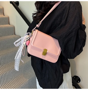 Detail of pink crossbody bag with gold buckle and lace heart charm on a black outfit