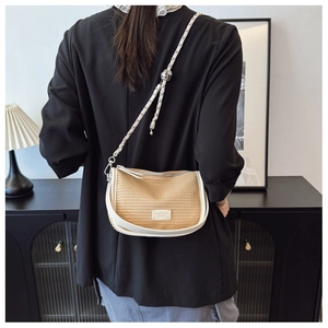 Detail of woven straw and white leather crossbody saddle bag with metal chain strap