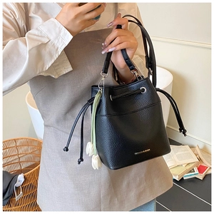 Detail of black bucket bag featuring lychee grain texture and tulip flower tassel charm