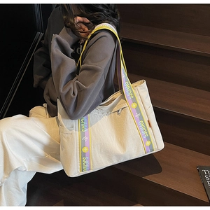Detail of off-white tote bag with floral wide strap on dark wooden stairs