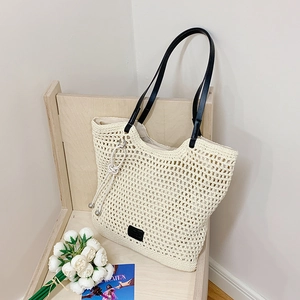 Detailed close-up of cream woven beach tote with black leather straps and leather patch