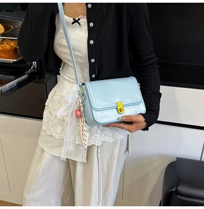 Detail of light blue crossbody bag with gold lock, pink heart charm and silk scarf decoration